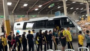 Jovens em fila ao lado de micro ônibus