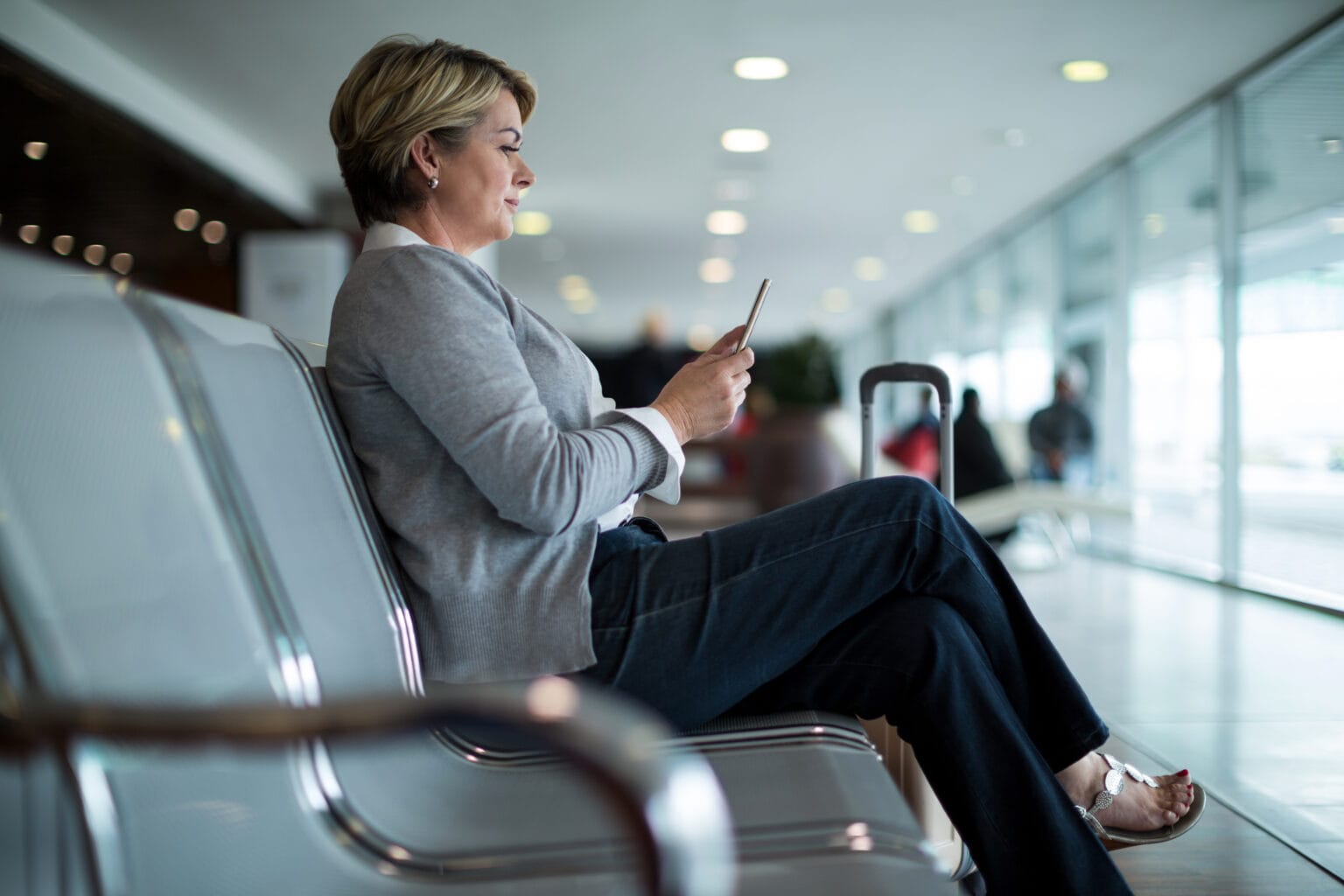 Mulher em cadeira de aeroporto mexendo em celular