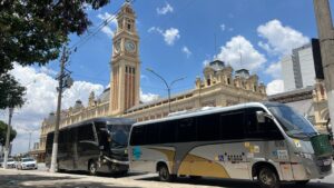Dois ônibus estacionados em frente a estação com relógio