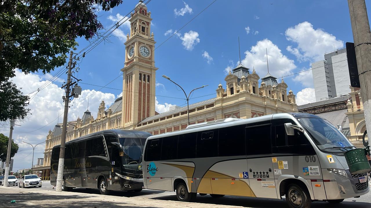 Dois ônibus estacionados em frente a estação com relógio