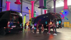 Crianças uniformizadas ao lado de ônibus e van estacionadas
